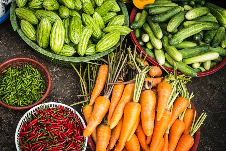 an overhead image of farmers market vegetables in bowls, including carrots, small hot peppers, and cucumbers