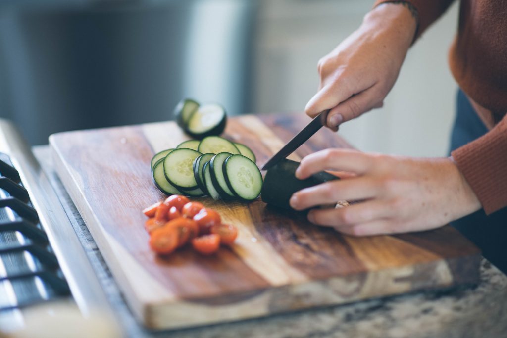 close up shot of cucumber being sliced on a wood cutting board