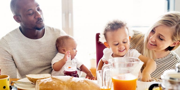 two smiling parents with two kids at the breakfast table with bread and juice