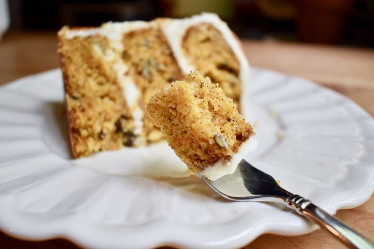 a slice of carrot cake with focus on a fork with a bite ready to eat