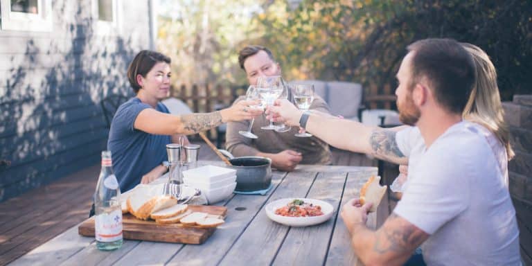 group of four young adults at an outdoor table, clinking glasses over a meal