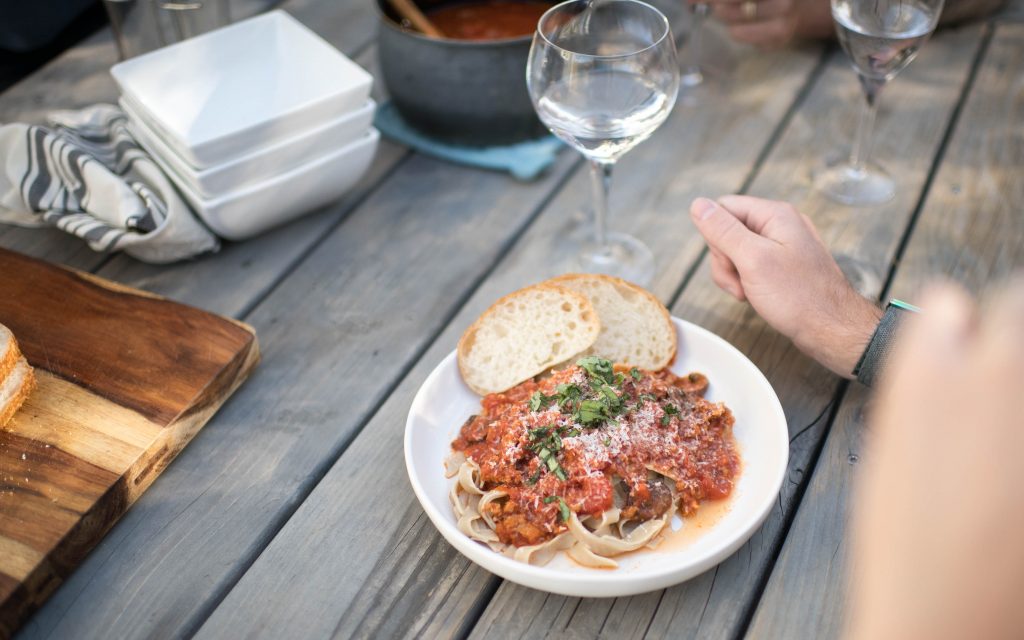 close up shot of spaghetti on a plate with a wine glass next to it