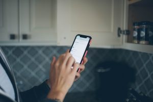 Cropped image of a hand holding a phone in a kitchen with a shopping list on screen