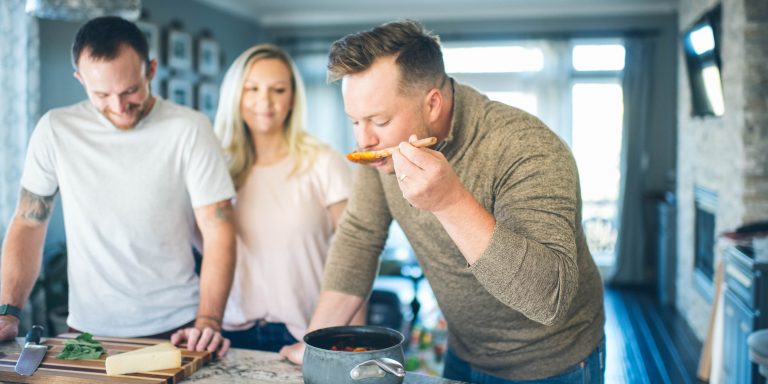 A young man tastes red sauce out of a saucepan