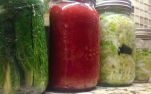 close up of three jars: homemade pickles, jam and sauerkraut 