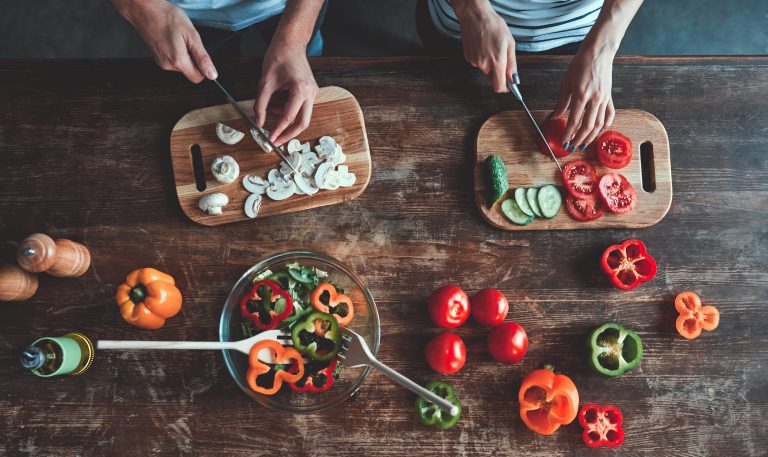 Cropped image of couple chopping vegetables on a wood table