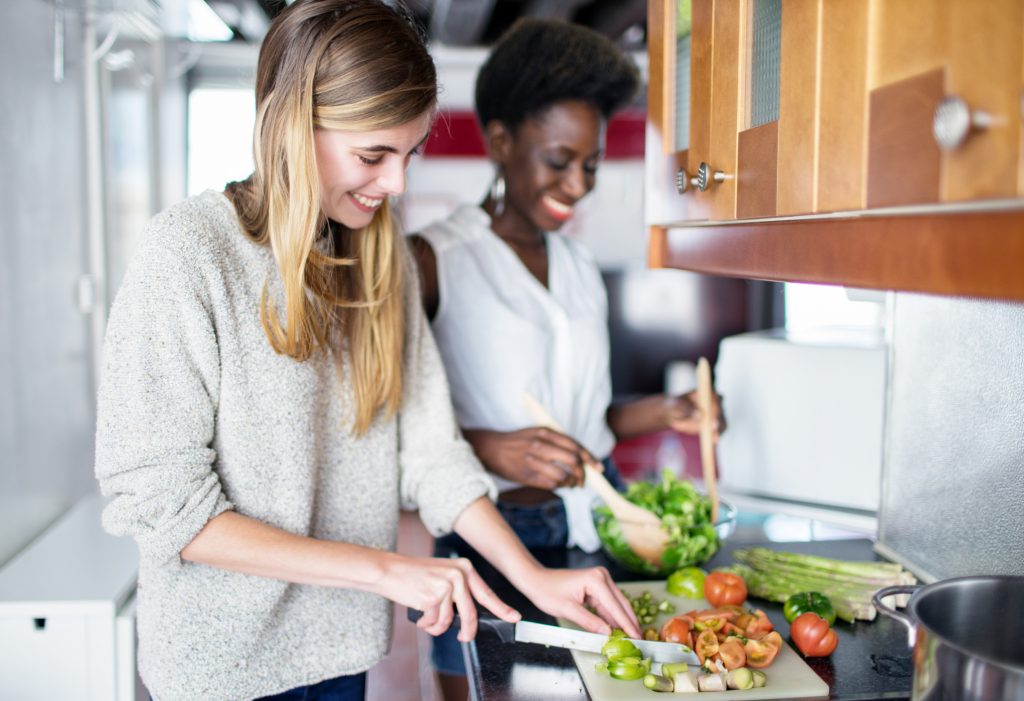 Two women chopping vegetables and mixing a salad in a kitchen