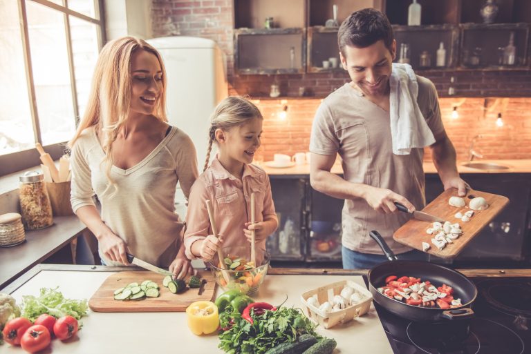 Little girl and her parents are smiling while cooking in kitchen at home