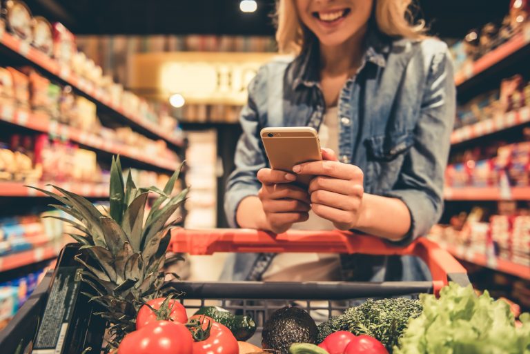 Cropped image of beautiful young woman using a smart phone and smiling while doing shopping at the supermarket