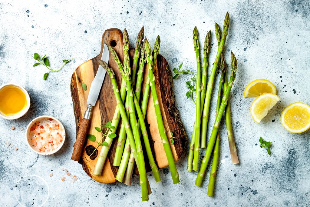 Bunch of fresh green asparagus on wooden board with olive oil, lemon and seasonings.