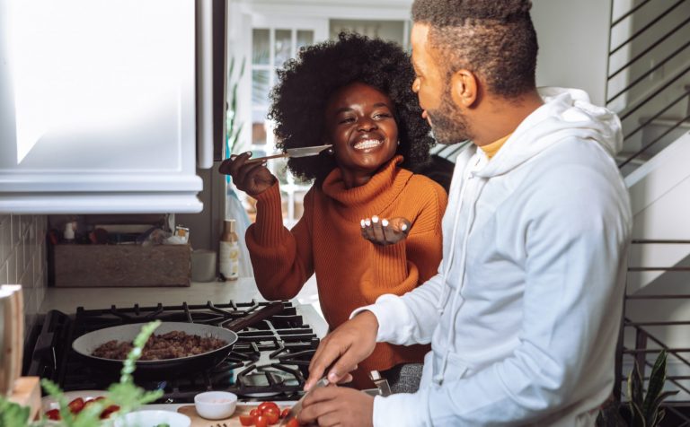 Two people smile at one another while cooking and chopping tomatoes in a kitchen