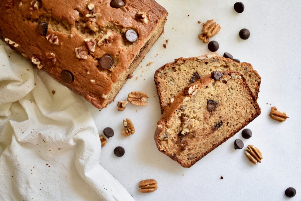 overhead shot of sliced banana bread loaf with chocolate chips scattered on white backround