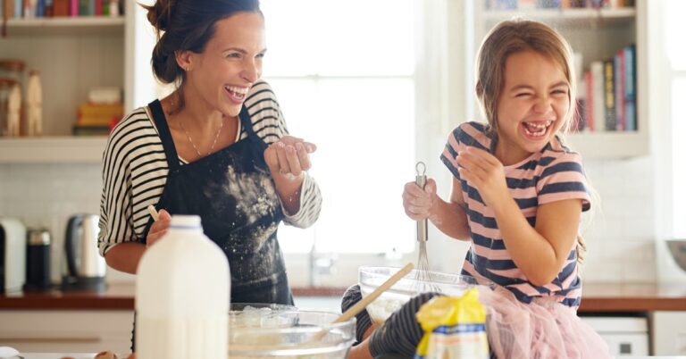 mom and daughter laughing and baking in the kitchen with clear glass bowls and whisks