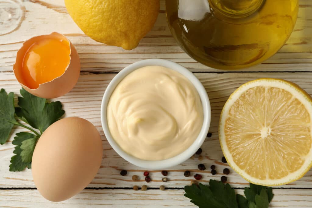 Bowl with mayonnaise and ingredients for cooking on wooden background