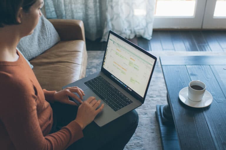 cropped image of woman working with her computer on her lap and a cup of coffee on the table