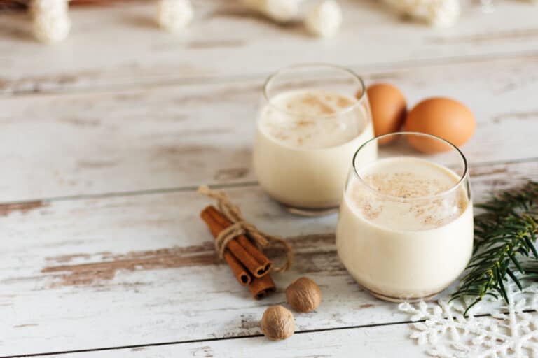 Fresh eggnog with cinnamon and nutmeg for christmas holiday with christmas decorations on wooden background..