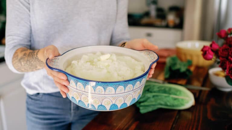 cropped image of woman holding blue and white ceramic pot filled with mashed potatoes