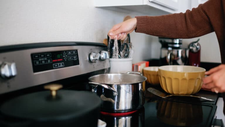 cropped image of a woman in a brown sweater adding salt to a pot of boiling water