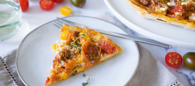 slice of upside down tomato tart on a white plate with full tart off to the upper right, scattered tomatoes around the plates