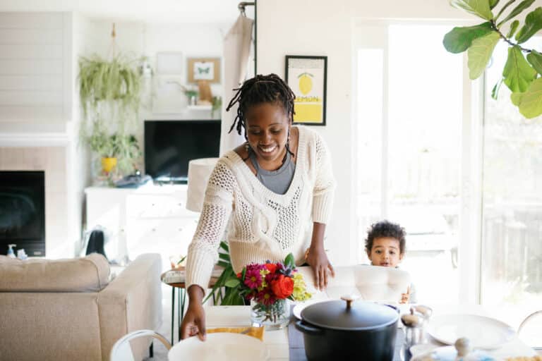 woman in a white sweater setting the table on a bright kitchen