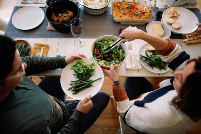 overhead view of two people at a dinner table passing a plate of green beans